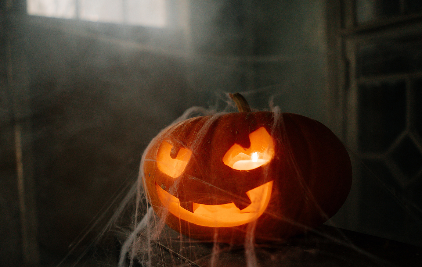 A spooky jack-o-lantern sitting in a dusty barn and covered in webs