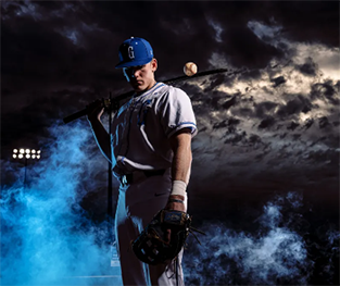 High school baseball player posing in front of a sky of blue and grey storm clouds