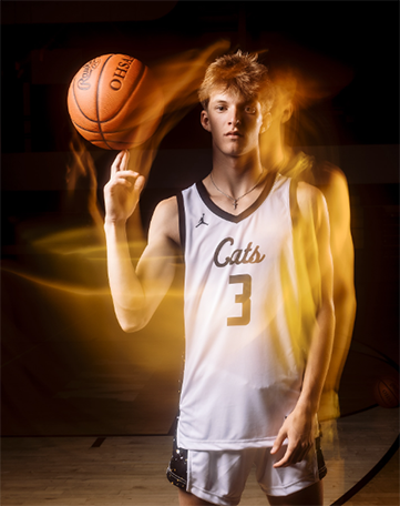 A high school basketball player standing up straight with a basketball on his finger, with motion blur around him.